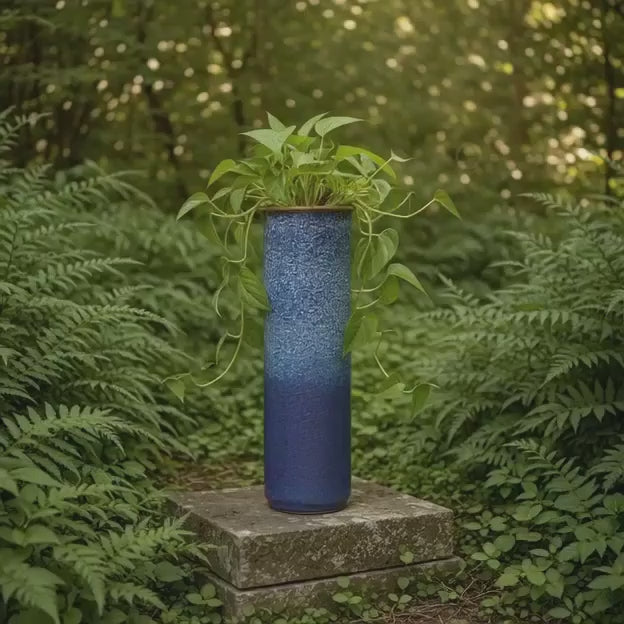 Tall reactive glaze ceramic planter showcasing cascading green foliage in a garden.
